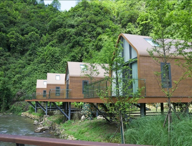A row of arched timber cabins raised beside a wooded stream