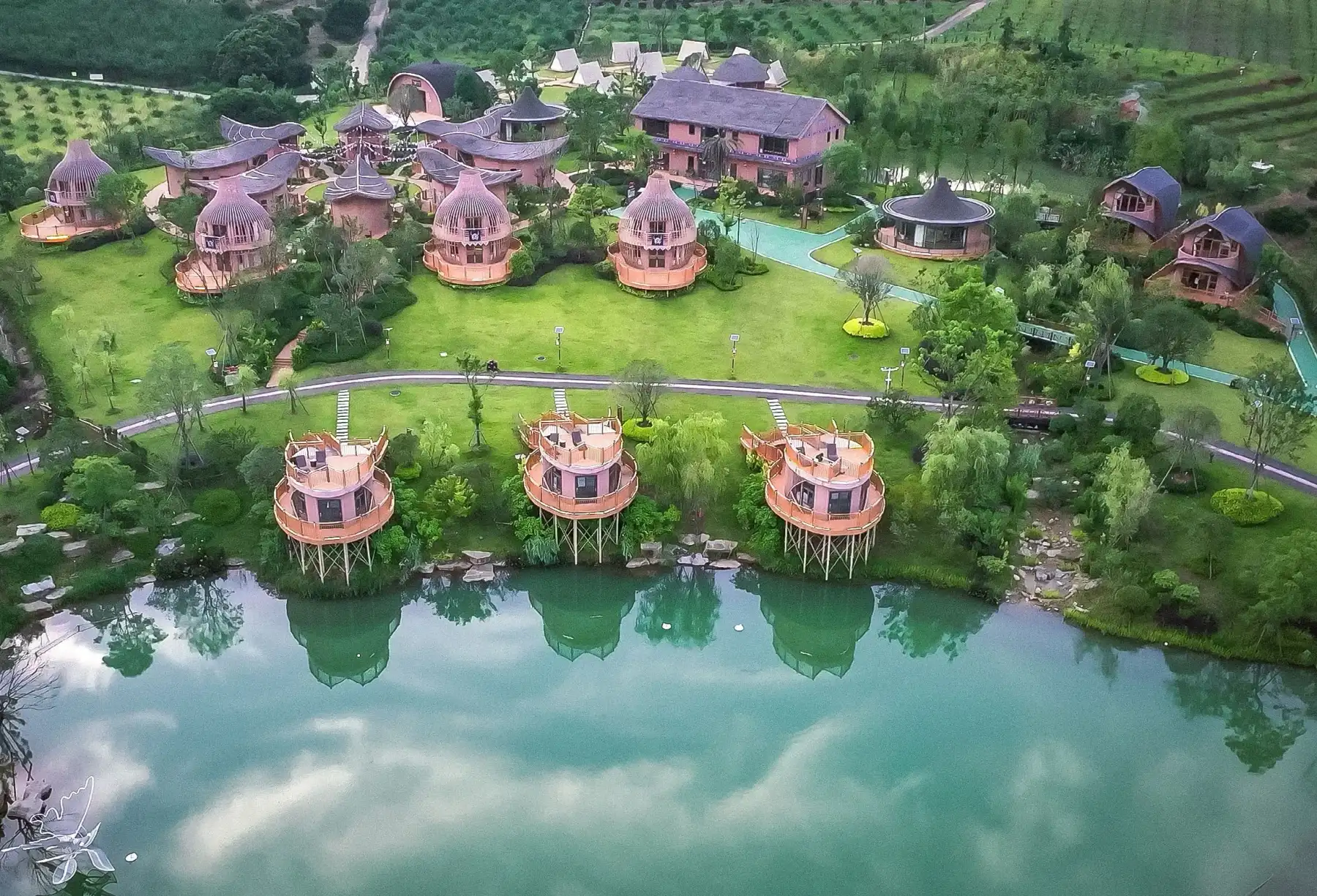 Aerial view of varied sculptural cabins arranged around lawns and water