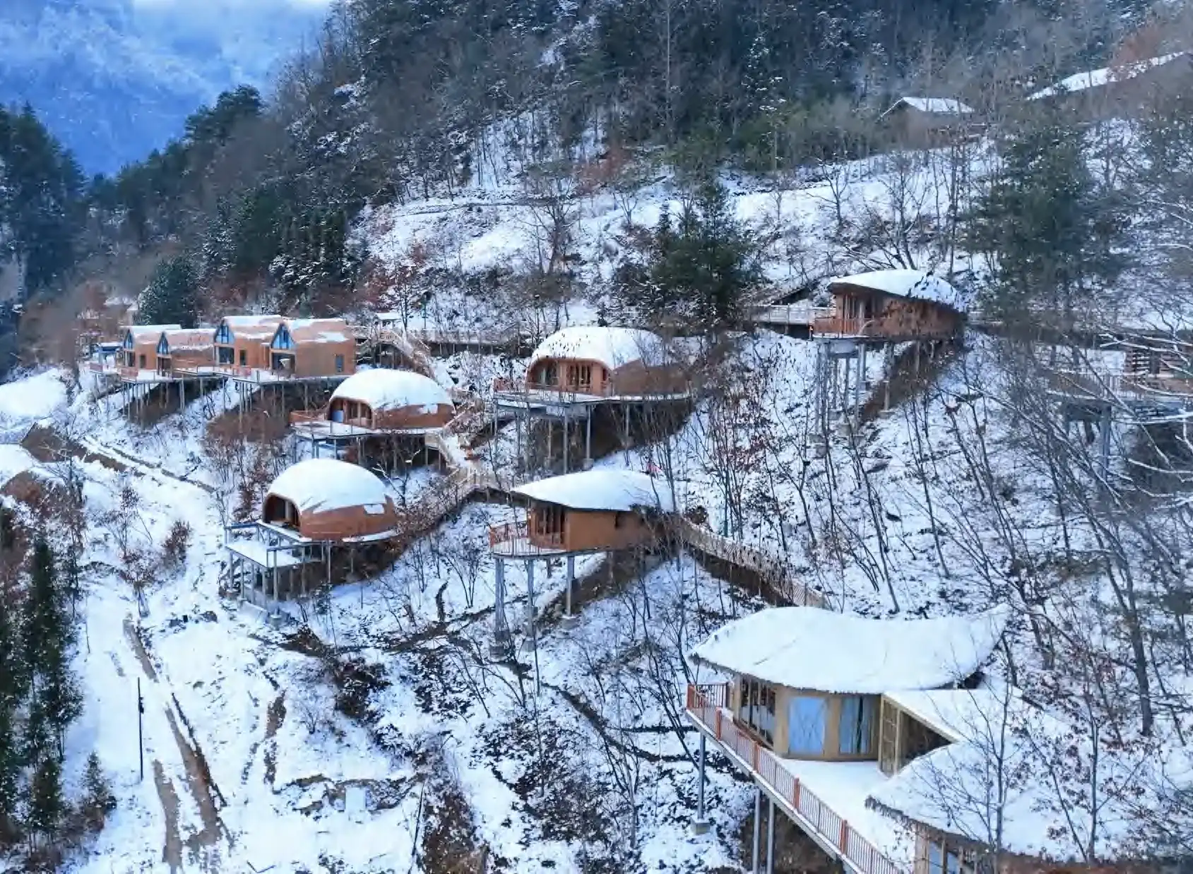 Curved timber guest pods connected by elevated walkways on a snow-covered hillside