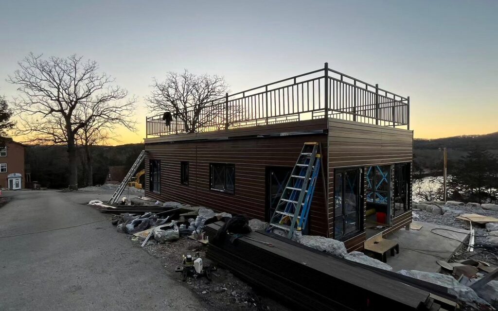 Real prefab steel-frame building site with road access, roof deck and exterior cladding progress